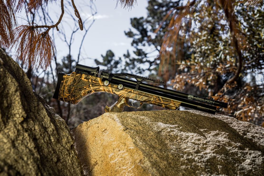 Camo stock aslekon rifle sitting on a large boulder.