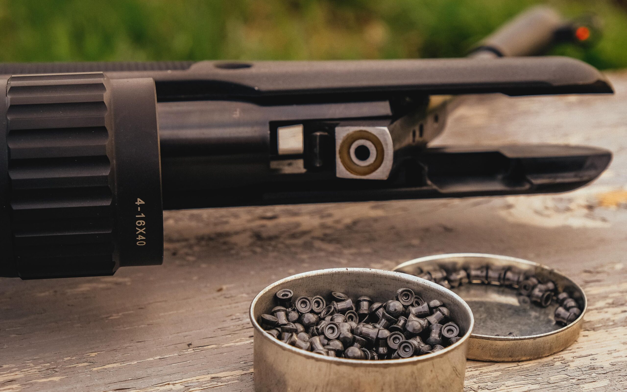 Close-up of an air rifle with a tin of pellets on a wooden surface.