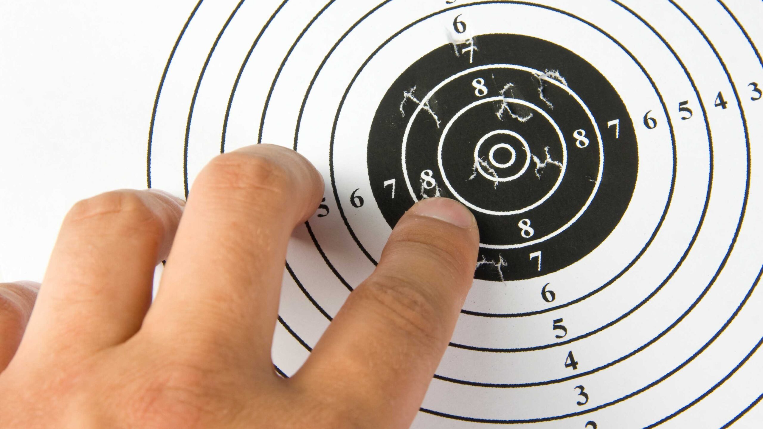 Close-up of a hand pointing at bullet holes clustered on a paper shooting target.